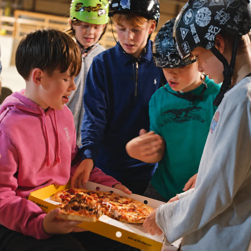 Barn med hjelmer deler pizza fra en gul Dolly-eske