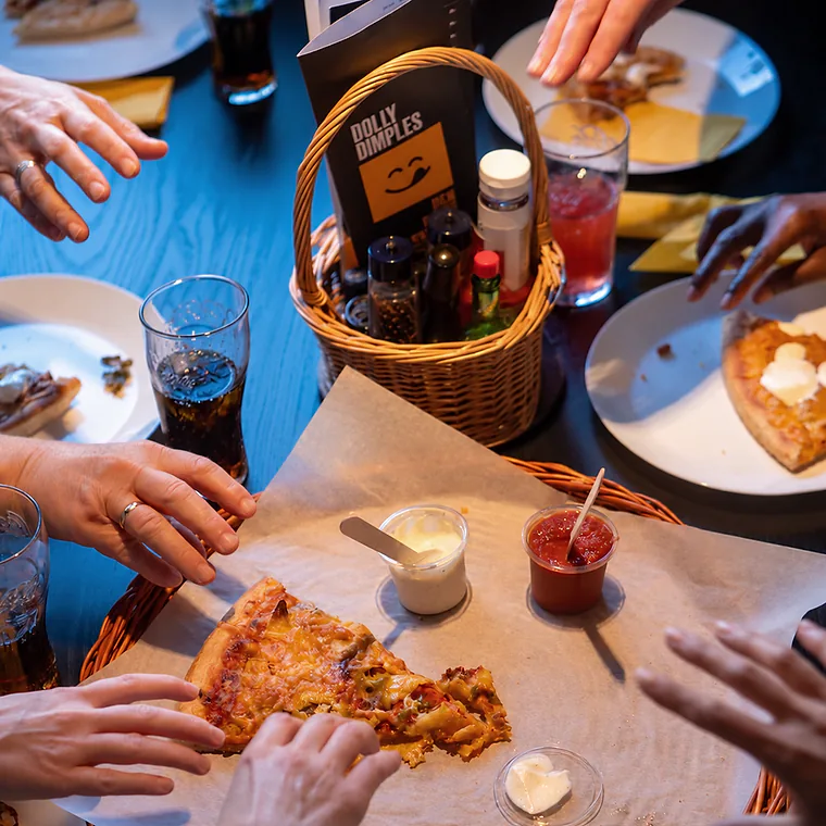 Hender rundt et bord med Dolly-pizza, dipp og drikke