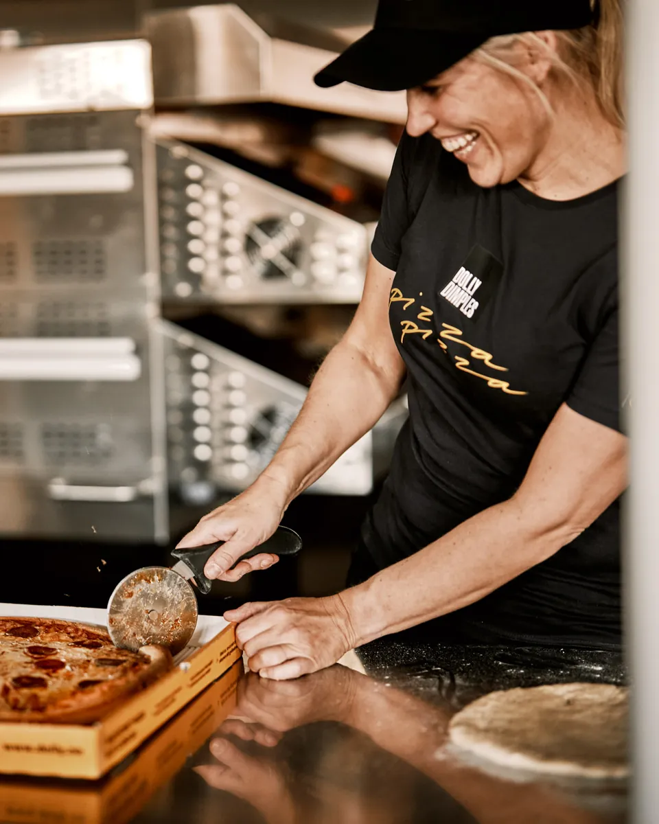 En smilende ansatt hos Dolly Dimples deler en pepperonipizza i en Dolly-eske