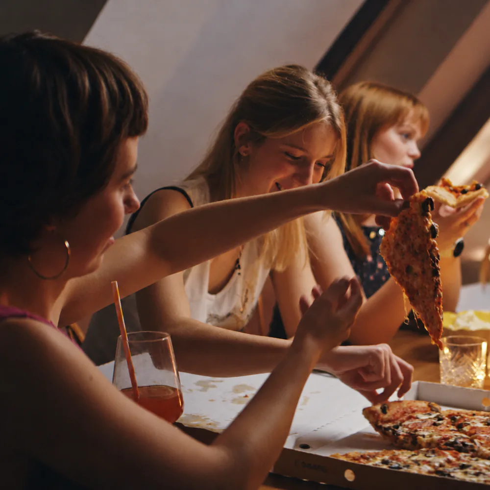 Tre venninner deler pizza rundt et bord med levende lys