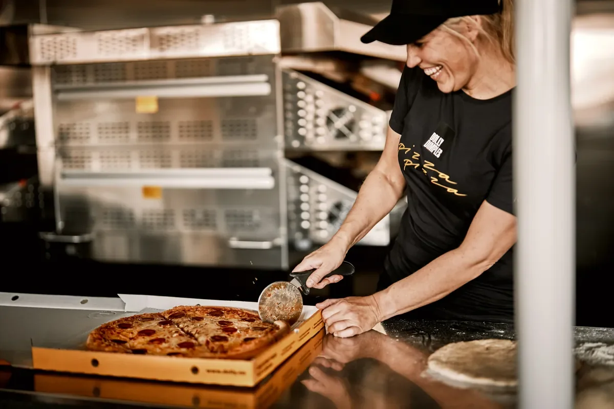 En smilende ansatt hos Dolly Dimples deler en pepperonipizza i en Dolly-eske